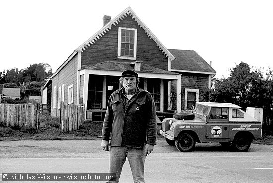 Byrd Baker, Mendocino sculptor and organizer of the Mendocino Whale War stands in front of his home, the red house on Ukiah St.  across from Corners of the Mouth food store in Mendocino. His classic Land Rover is painted with anti-whaling slogans such as "Stop the Slaughter" and "Boycott Japanese Products." Photo © 1976 Nicholas Wilson, PO Box 943, Mendocino CA 95460, negative  2/8/76-A25, scanned from 35mm neg at 2700 dpi, Nikon LS-2000.