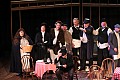 Townspeople (chorus) look on in amusement as Alcindora is stuck with the bill.