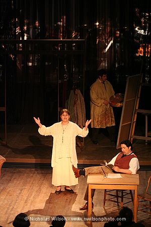 Narrator Lorry Lepaule sets the scene, back in the bohemian garret studio in Act IV of La Boheme. The orchestra can barely be seen in the background behind a sheer curtain.